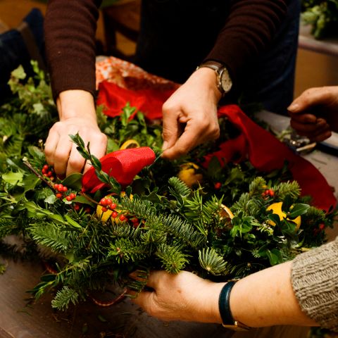 close up image of two pairs of hands creating a Christmas wreath 